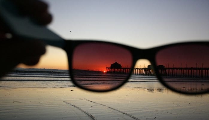 A pair of sunglasses on the beach at sunset.